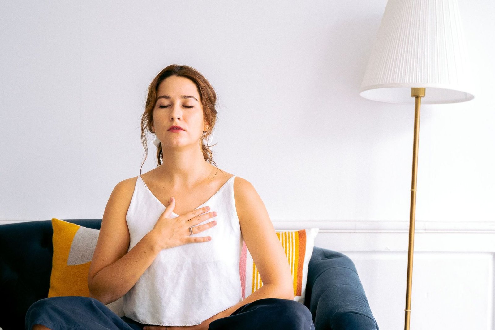 Mujer sentada en el sofá con los ojos cerrados y la mano en el pecho, recibiendo Reiki a distancia en casa