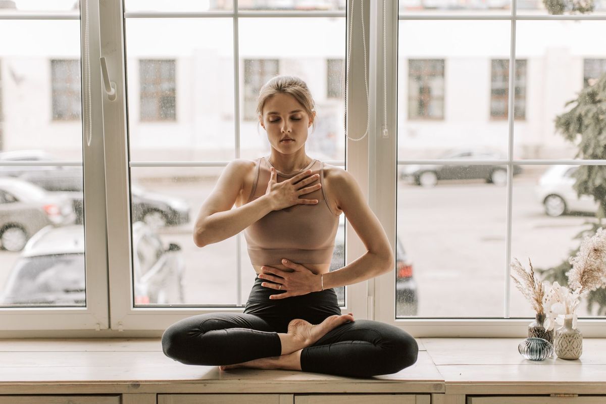 Mujer con las manos sobre el pecho junto a una ventana, autotratamiento de Reiki Nivel 1