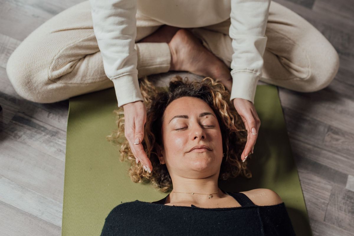Manos de una practicante de Reiki junto a la cabeza de una persona tumbada, sesión de Nivel 2
