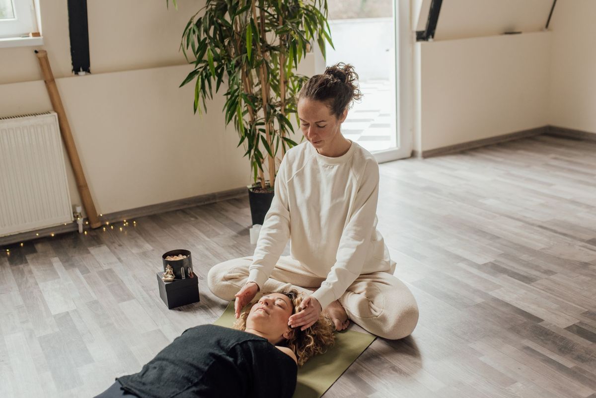 Practicante de Reiki con las manos sobre la cabeza de una persona tumbada en una sala luminosa